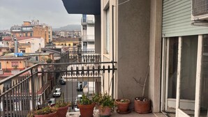 Ein Balkon mit Blumentöpfen, einem Metallgeländer und Blick auf die Stadtlandschaft.
