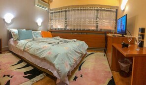 A bedroom with a bed, a desk, a chair, a television, and a window with blinds. - Room-hotel Square Macedonia (Skopje)