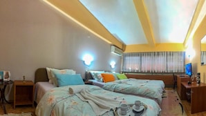 A hotel room with two beds, a bedside table with books, a TV, and a bathroom with a sink and mirror.