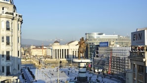 A public square with a central statue, surrounded by classical architecture and modern buildings.