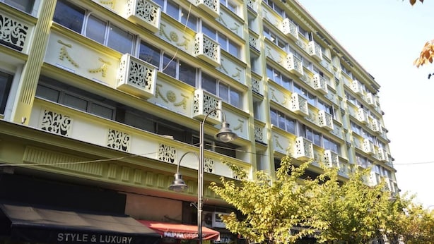 A multi-story building with balconies, storefronts, and a tree in front.