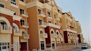 Un edificio residencial de varios pisos con balcones, vista a la calle y cielo despejado.
