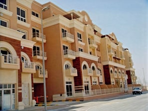 Edifício residencial com vários andares, varandas, vista para a rua e céu claro.