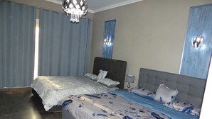 Un dormitorio con una cama grande, una mesita de noche, una araña y una ventana con cortinas.