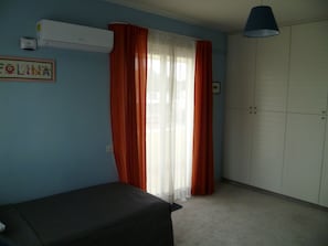 A room with a bed, an air conditioning unit, a wardrobe, and a window with curtains.