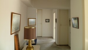 Um corredor com um abajur, quadros nas paredes e uma porta no final.