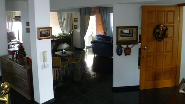 Uma sala de estar com área de jantar, uma porta decorada com uma coroa de flores e escadas que levam a outro andar.
