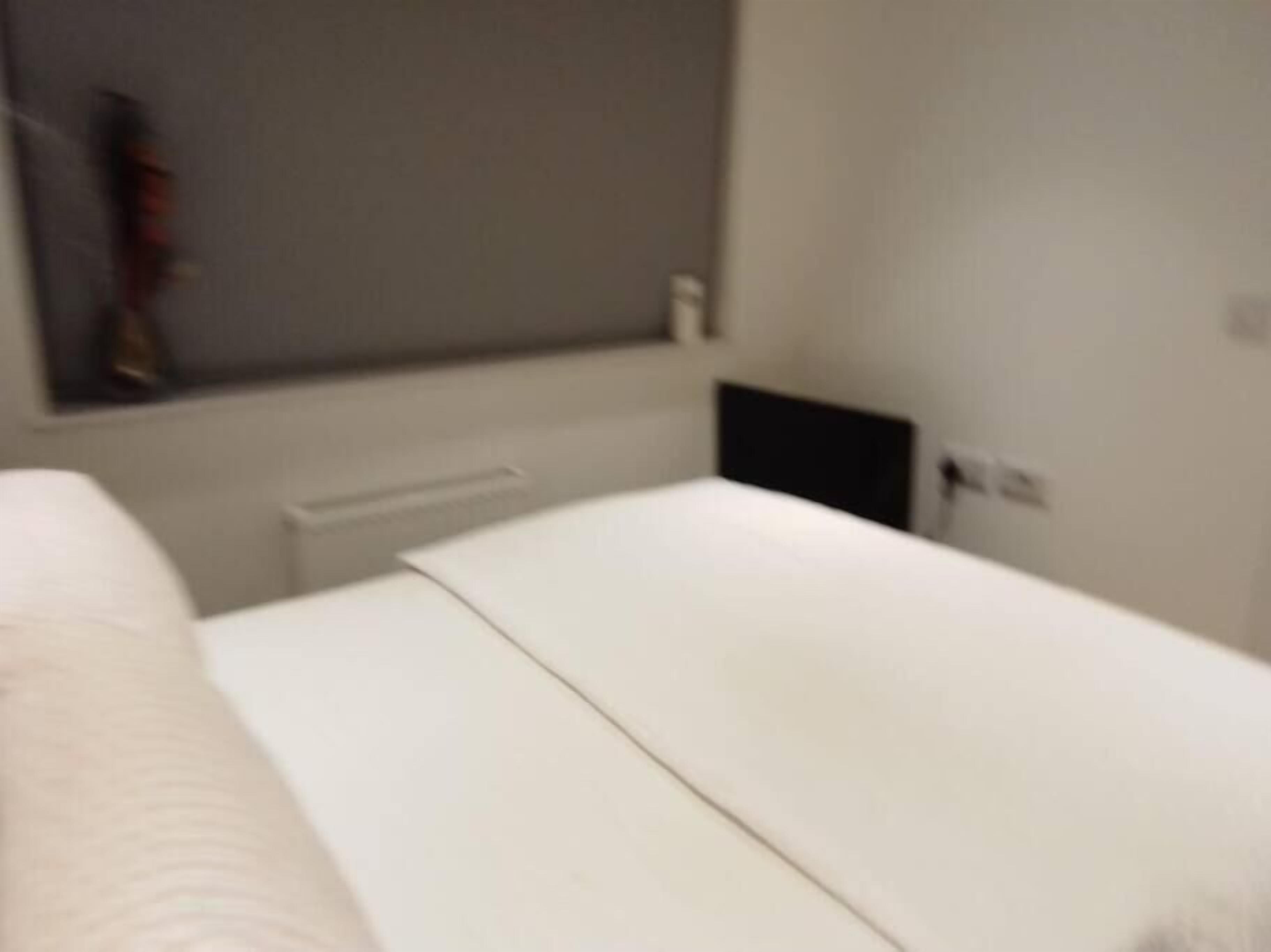 A room with a bed, a radiator, a wall-mounted shelf, and a power outlet.