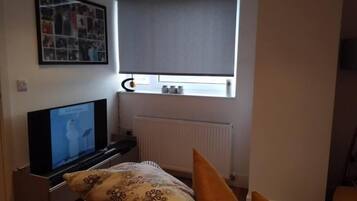 Un dormitorio con cama, televisión, ventana con persianas y radiador.