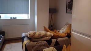 Un soggiorno con divano, cuscini, termosifone, finestra e lampada.