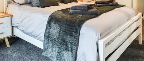 Un lit bien fait, avec une tête de lit blanche, une armoire en bois et une petite table de chevet dotée d’un tiroir.