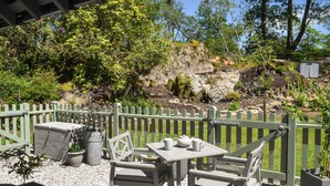An outdoor seating area with a table and chairs, surrounded by a green fence, and a rocky backdrop. - 1 bedroom accommodation in Windermere and Troutbeck Bridge (Windermere and Troutbeck Bridge)