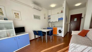 Habitación de hotel compacta con cama, escritorio con computadora, lavadora y pequeña kitchenette.