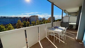 Un balcón con mesa y sillas, un equipo de aire acondicionado y vistas a edificios y árboles.
