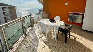 Un balcon avec une table et des chaises, une vue sur la mer et un appareil de climatisation.