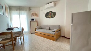 Un espace de vie compact comprenant un canapé, une table à manger avec des chaises, un four à micro-ondes, un réfrigérateur et une horloge murale.