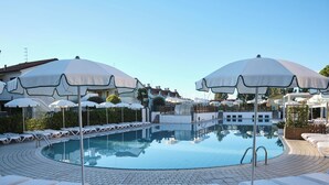 Un espace piscine doté de chaises longues et de parasols, entouré d’immeubles.