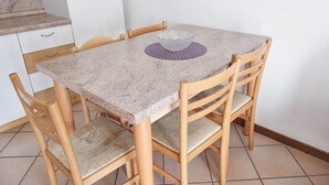 Une petite table à manger sur laquelle repose un saladier en verre, le tout posé sur un set de table violet, et entouré de chaises en bois dotées d’assises rembourrées.