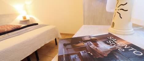 A neatly made bed with a white comforter and a pillow, a bedside lamp, and a magazine titled "SALENTO Style" on a table.