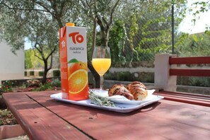 Jugo de naranja envasado, un vaso de jugo de naranja y croissants sobre una mesa al aire libre.