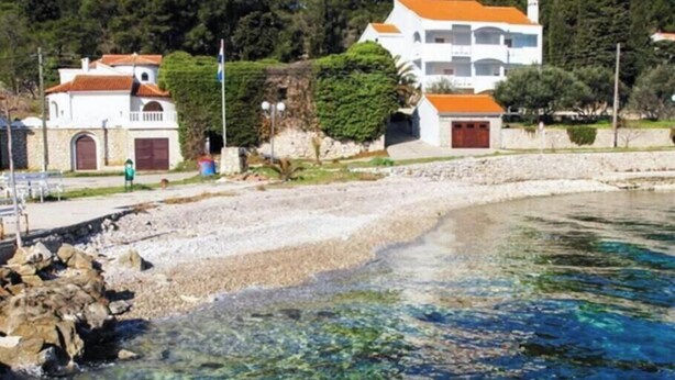 Um imóvel costeiro com edifícios brancos, uma praia rochosa e céu azul claro.