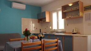 Uma cozinha compacta com uma mesa de jantar, cadeiras, geladeira e janela.