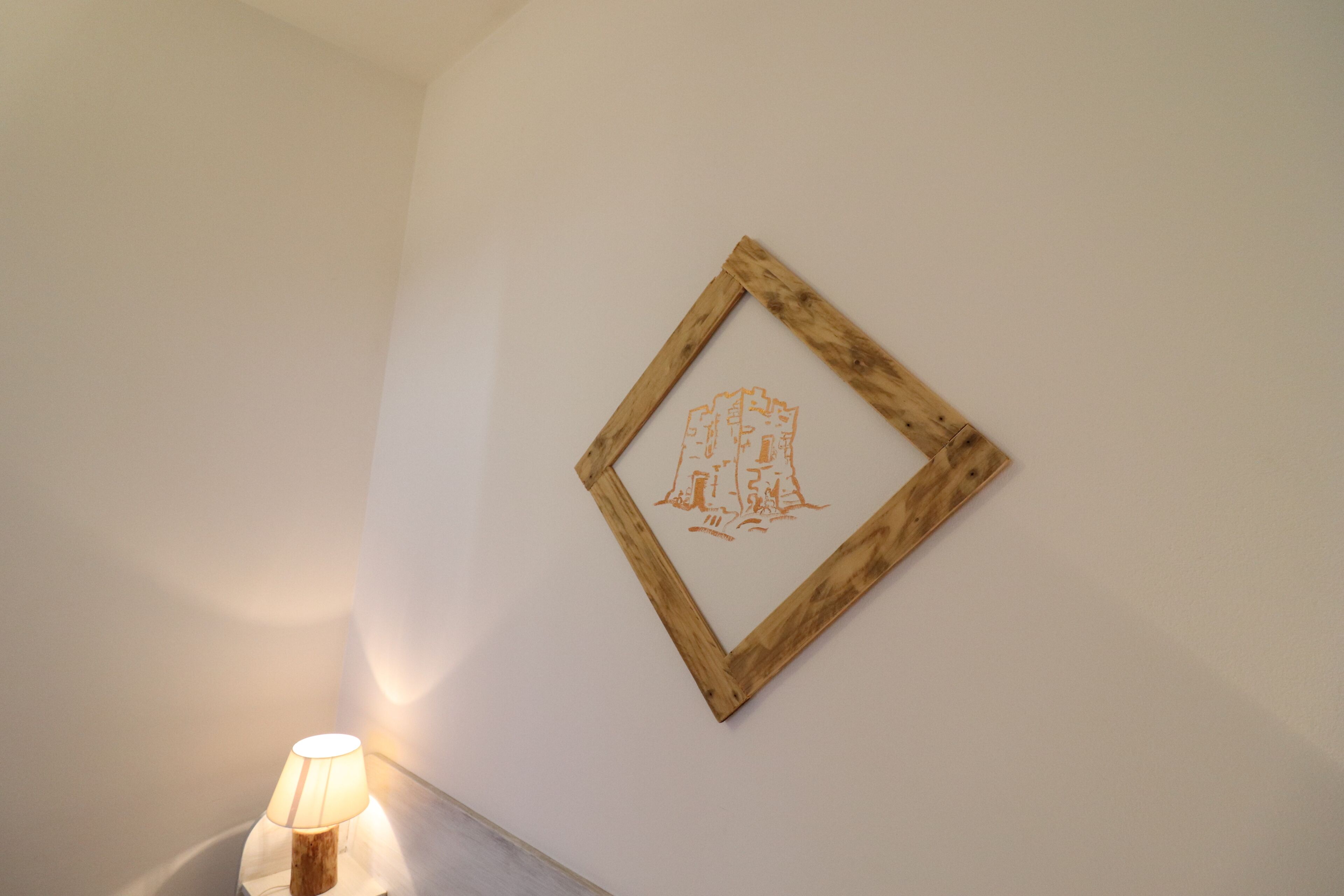 Ein gerahmtes Kunstwerk an der Wand, eine Lampe auf einem Beistelltisch und eine schlichte Wand.