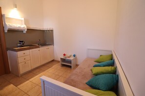 A small, compact room with a kitchenette, a single bed with colorful pillows, and a small nightstand. - Casa Regina Residence Torre Santo Stefano in Otranto 3 Places (Otranto)