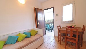 Ein Zimmer mit einer Couch, einem Esstisch, Stühlen, einem Fenster und einer zur Außenseite führenden Tür.