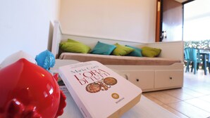 Un livre intitulé « L’ORA DI TUTTI » est posé sur une table dans une pièce bien éclairée, avec un canapé et des fauteuils en arrière-plan.