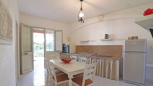A kitchen with a dining table, chairs, a refrigerator, a sink, and a window with a view of greenery. - Casa Primus Torre Santo Stefano in Otranto (Otranto)