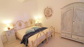 A bedroom with a bed, bedside tables, a wardrobe, and a decorative wall piece. - Casa Primus Torre Santo Stefano in Otranto (Otranto)