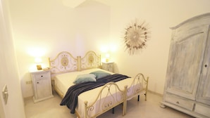 A bedroom with a bed, bedside tables, a wardrobe, and a decorative wall piece. - Casa Primus Torre Santo Stefano in Otranto (Otranto)