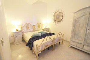 A bedroom with a bed, bedside tables, a wardrobe, and a decorative wall piece. - Casa Primus Torre Santo Stefano in Otranto (Otranto)