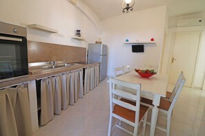 Eine Küche mit Herd, Backofen, Kühlschrank und einem Esstisch mit Stühlen.