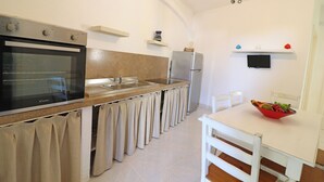 A kitchen with a built-in oven, a refrigerator, a sink, and a dining table with chairs. - Casa Primus Torre Santo Stefano in Otranto (Otranto)