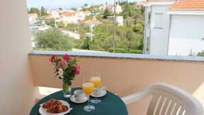 Un balcon avec une table préparée pour le petit-déjeuner, comprenant des croissants, du jus de fruits et un vase de fleurs.