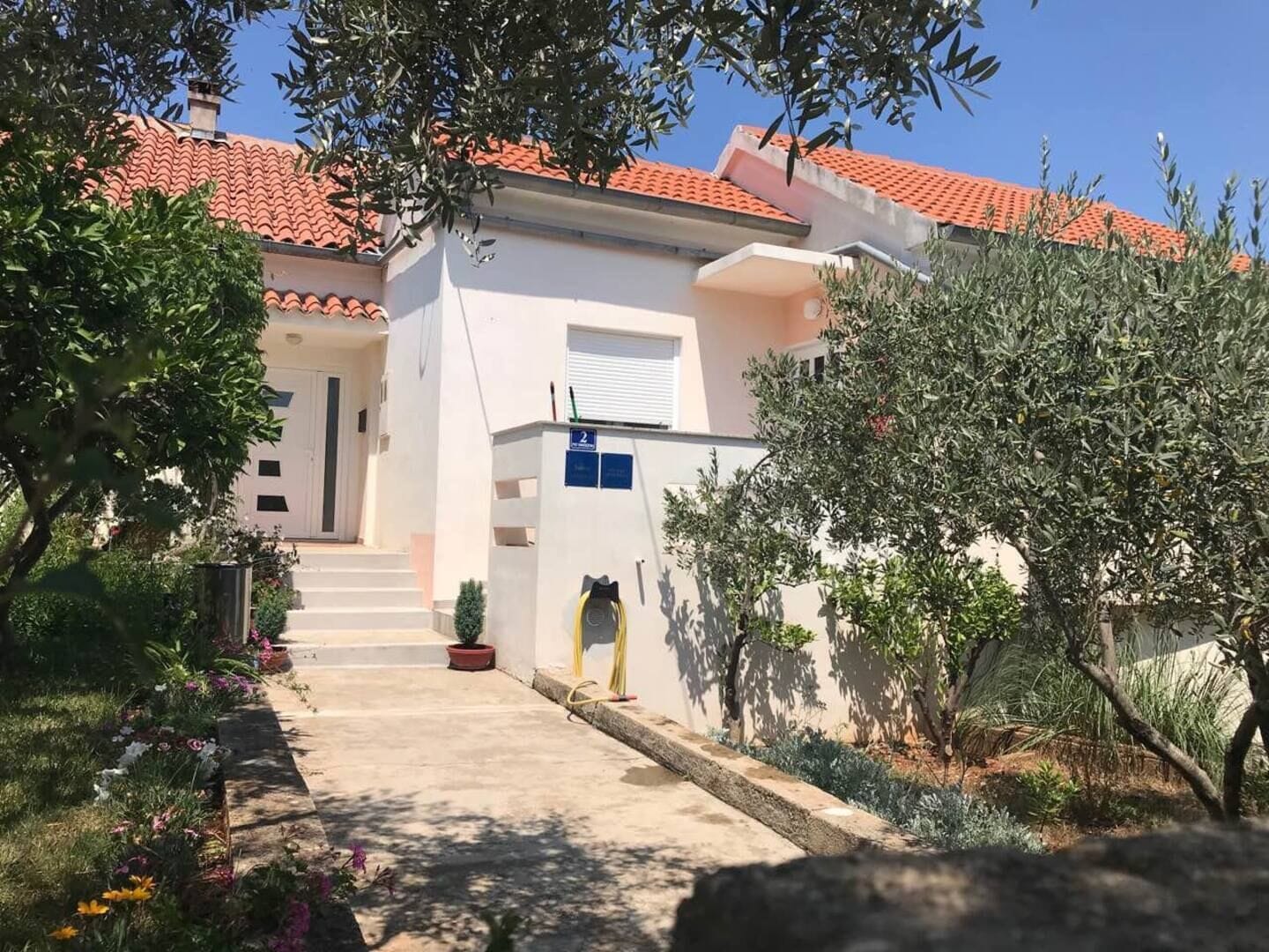 A building with a red-tiled roof, a white exterior, and a garden with various plants and flowers.