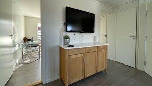 A modern kitchen with a flat-screen TV, wooden cabinets, and a glass dining table. - Bnb Stavanger Ap 9 Bertis "rooftop Terrace" (Stavanger)
