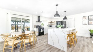 A modern kitchen with white cabinetry, a central island, and wooden chairs. - NEW 15% DISCOUNT❤Stock Tank Pool❤Hot Tub❤Game Room (Joshua Tree)