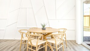 A room with a round wooden table surrounded by six woven chairs, a small potted plant on the table, and a white wall with geometric patterns. - NEW 15% DISCOUNT❤Stock Tank Pool❤Hot Tub❤Game Room (Joshua Tree)