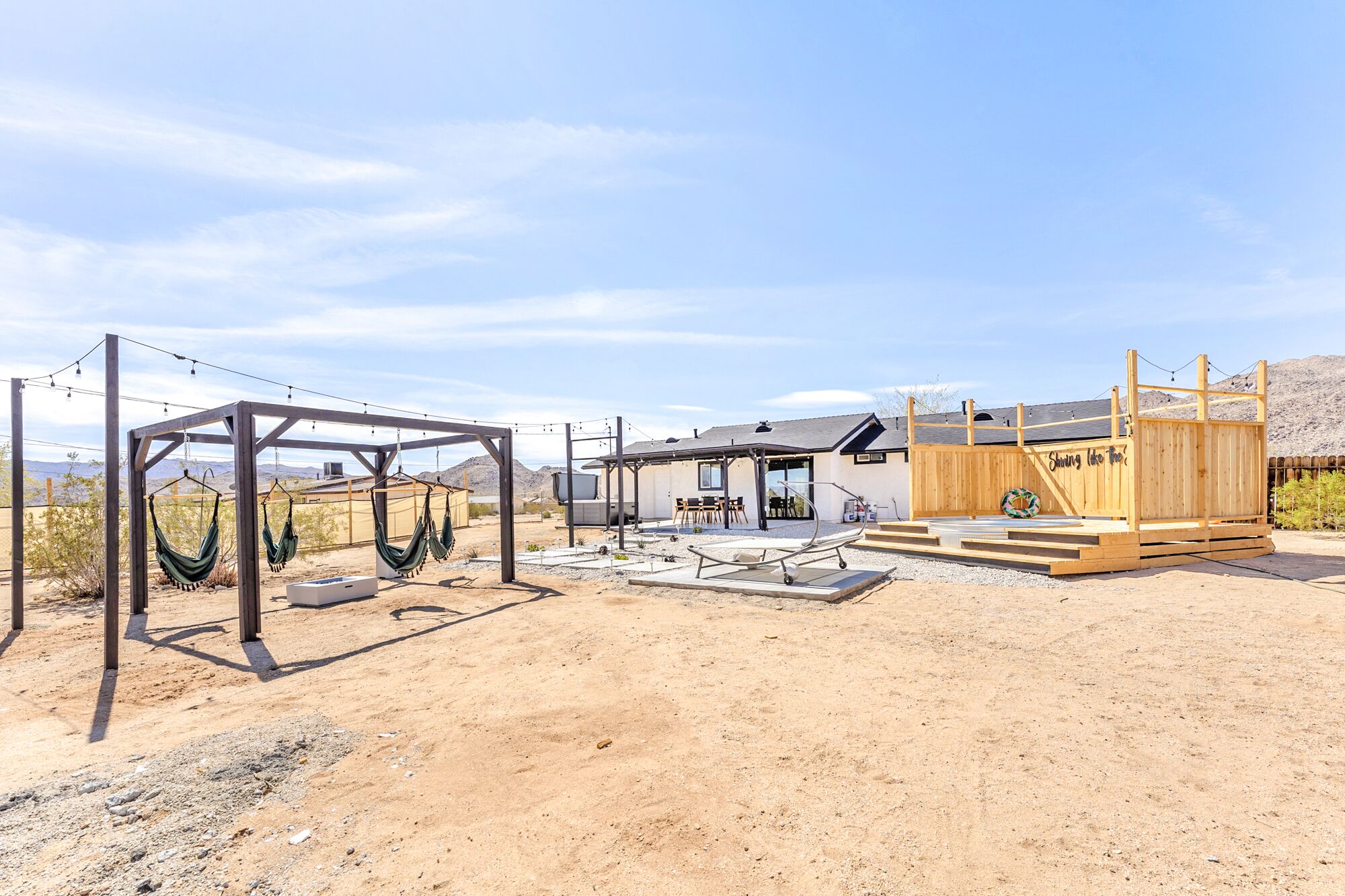 A desert-style outdoor area with hammocks, a wooden deck, and a small building with a covered seating area.