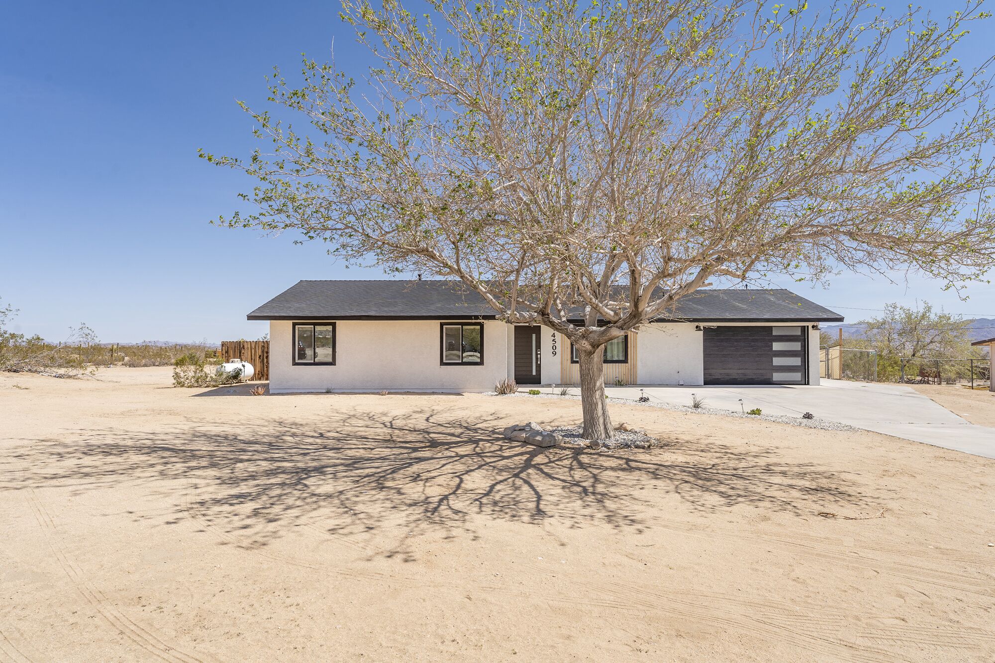 A single-story house with a garage, a tree in front, and a clear sky.