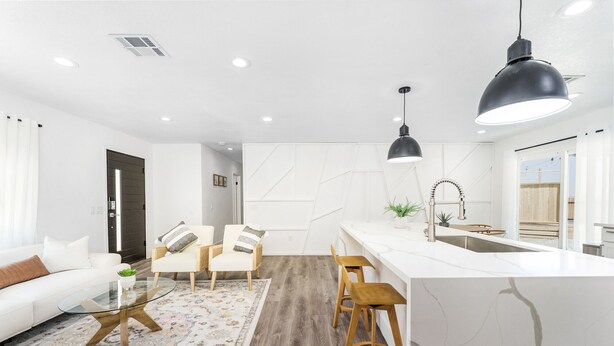 A modern kitchen with white cabinetry, a marble countertop, and a black pendant light. There is a wooden dining table with chairs and a white sofa in the living area. - NEW 15% DISCOUNT❤Stock Tank Pool❤Hot Tub❤Game Room (Joshua Tree)