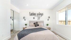 A bedroom with a bed, two bedside tables, a wall-mounted light, a window, and a wall decoration. - NEW 15% DISCOUNT❤Stock Tank Pool❤Hot Tub❤Game Room (Joshua Tree)