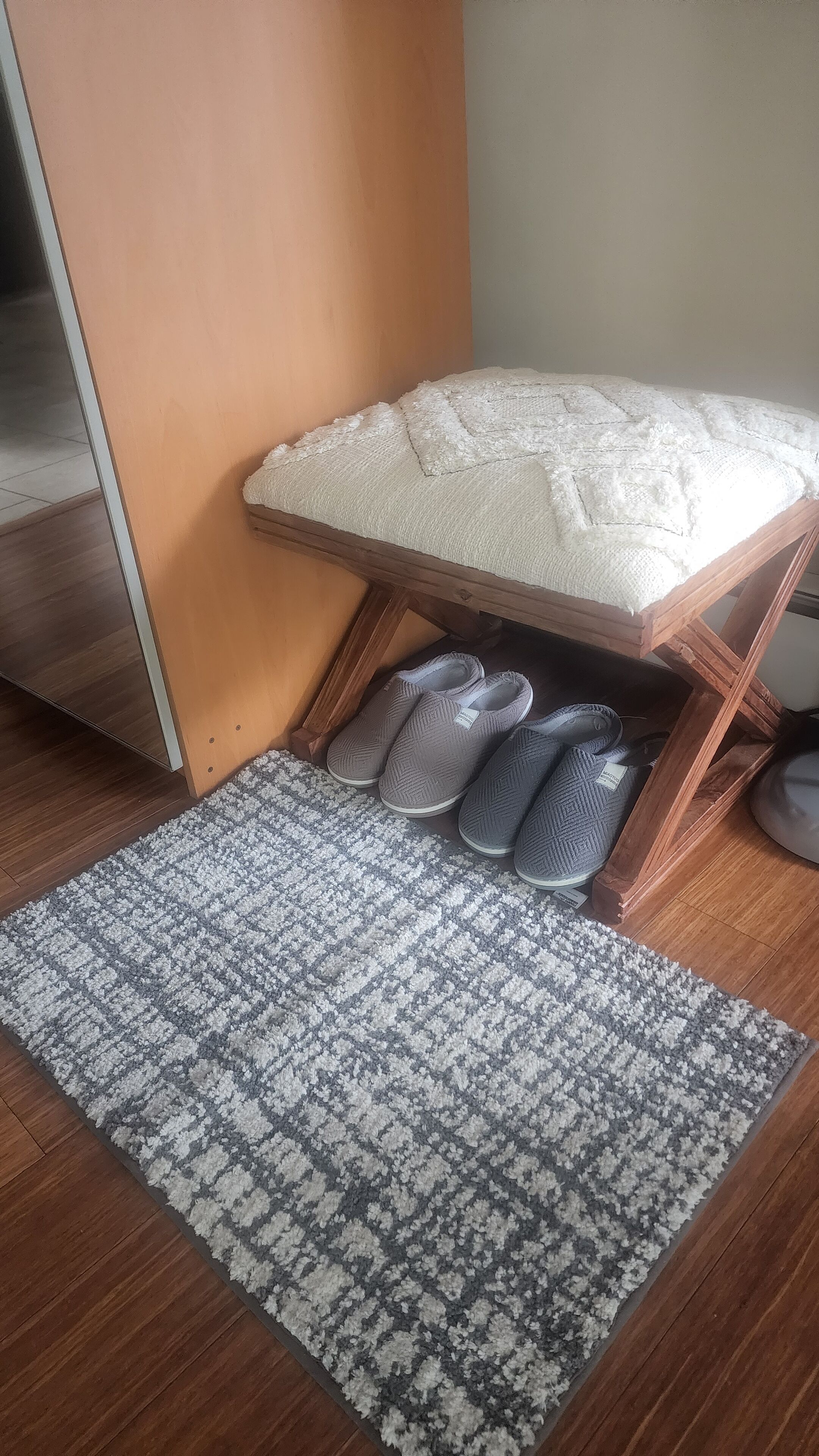 A corner of a room with a wooden bench, a patterned rug, and a pair of slippers.
