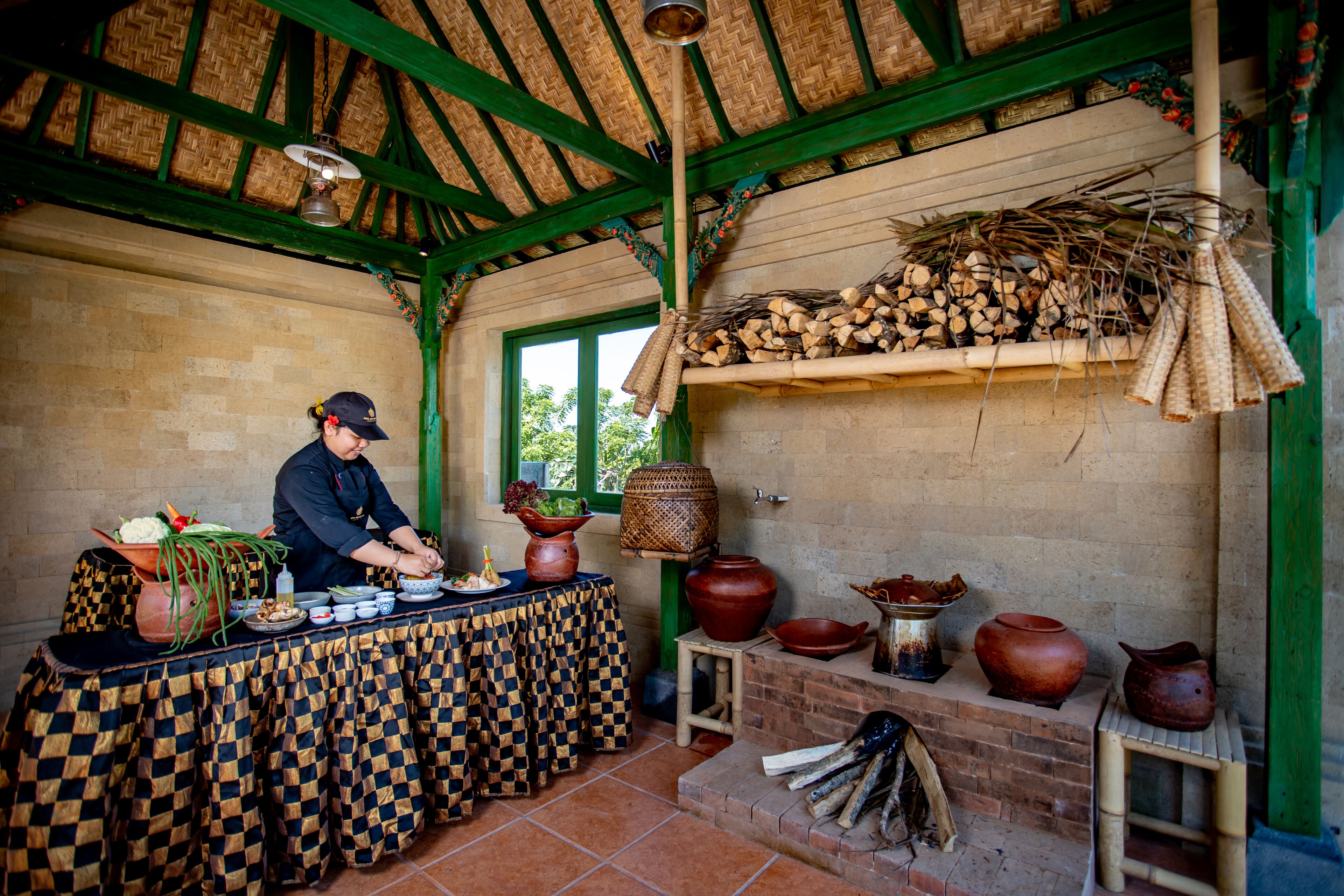 A kitchen with a checkered tablecloth, a chef preparing food, and various cooking utensils and pots on shelves.