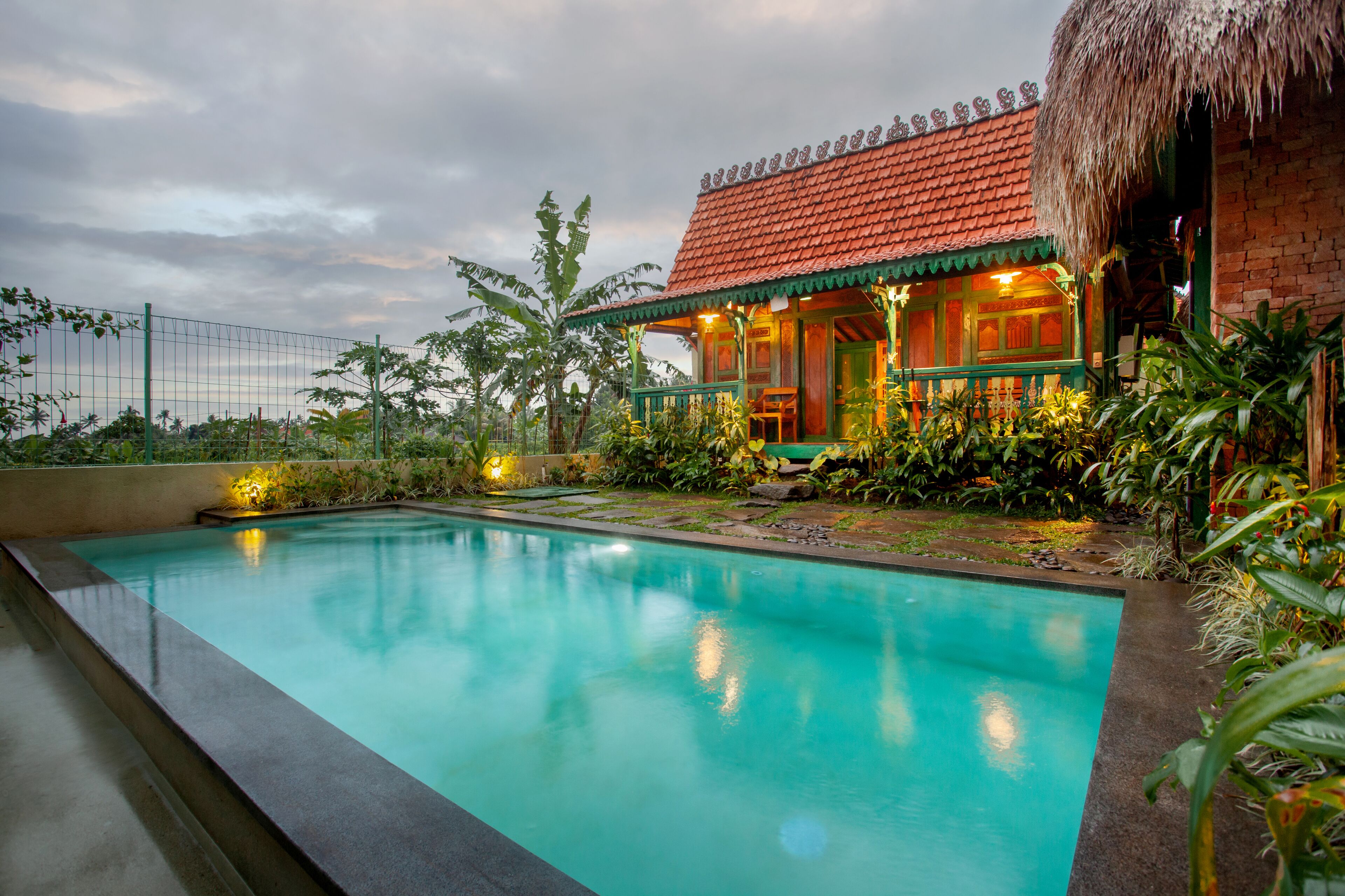 A swimming pool with a thatched-roof building adjacent to it.