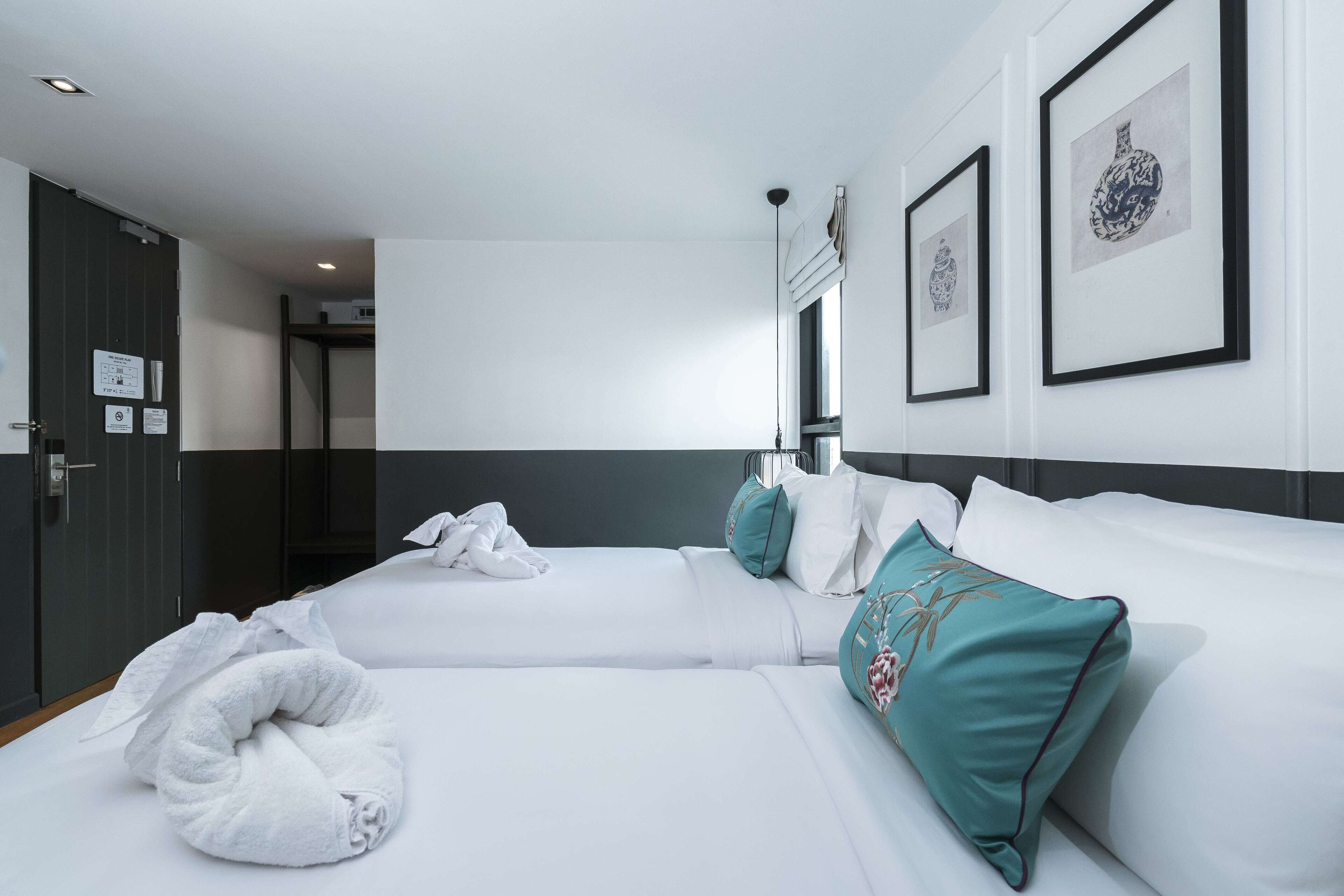 Una habitación de hotel con dos camas, ropa de cama blanca, almohadas color turquesa y cuadros en la pared.