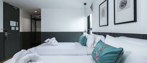 Una habitación de hotel con dos camas, ropa de cama blanca, almohadas color turquesa y cuadros en la pared.